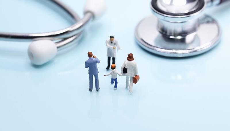 Miniature people: family standing in front of colorful pills and stethoscope on blue background with copy space. Health care, medical service, and insurance concept