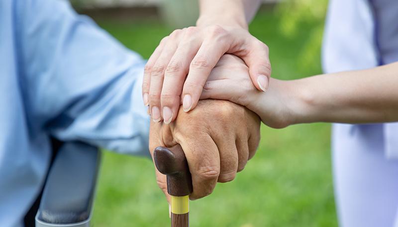 Nurse holding elderly man hand with cane on wheelchair in garden close up