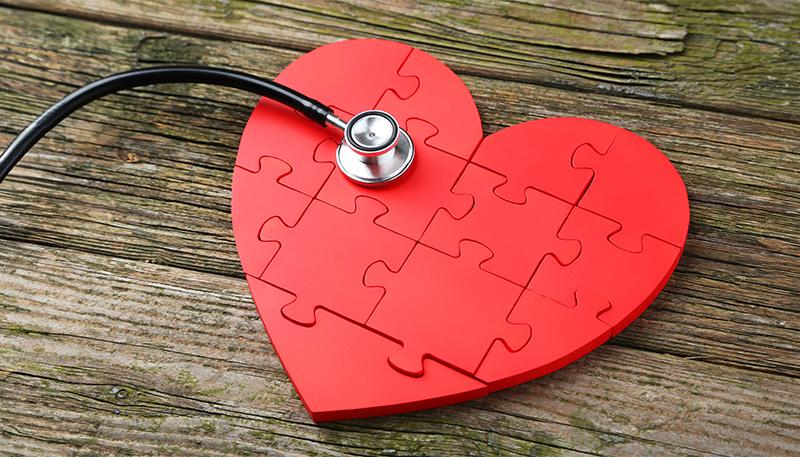 Red puzzle heart with stethoscope on wooden background